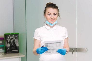 Elinde belgeler le genç kadın diş hekimi klinikte duruyor