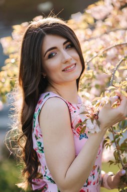 Güzel elbiseli zarif kadın parkta pembe ağacın yanında duruyor