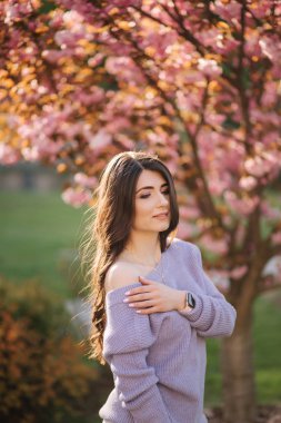 Parktaki sakura ağacının önünde mor bir kazak standında çekici genç kadın