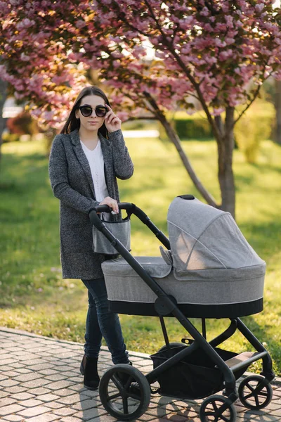 Young mom walking in the park with her baby in stroller