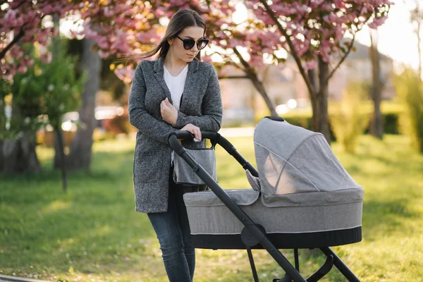 Young mom walking in the park with her baby in stroller