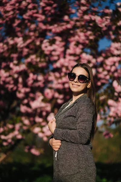 Жінка-бійка в блістері і сонцезахисних окулярах стоїть перед рожевим деревом — стокове фото