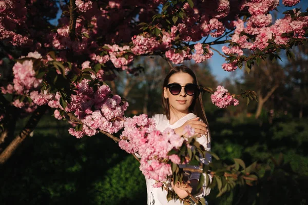 Hermosa mujer en gafas de sol de pie en el árbol de sakura —  Fotos de Stock