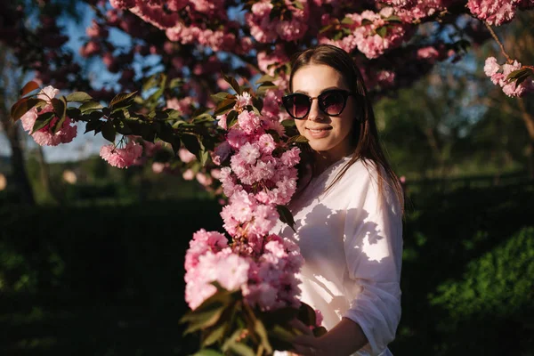 Schöne Frau mit Sonnenbrille steht im Sakura-Baum — Stockfoto