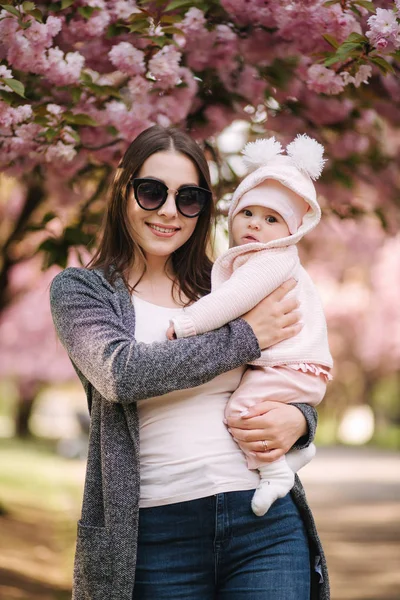 Küçük kızıyla güzel bir anne. Güneş gözlüksi takan annem. Pembe ağacın arka planı