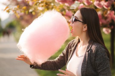 Pembe sakura ağacının önünde pamuk şeker yiyen çekici genç kızın yakın portresi