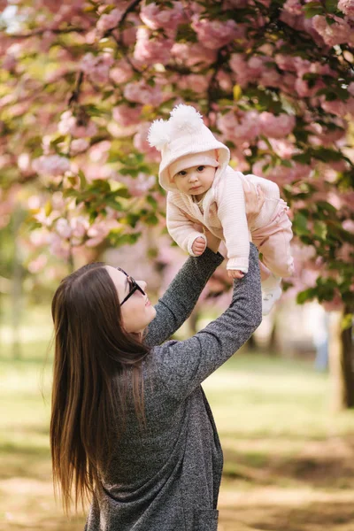 Vista laterale di felice giovane madre che tiene la bambina tra le mani e la guarda con amore — Foto Stock