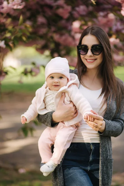 Όμορφη μαμά περπατάει με το κοριτσάκι της στα χέρια στο πάρκο. Ροζ φόντο — Φωτογραφία Αρχείου