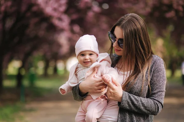 Beautiful mom walk with her baby girl on hands in the park. Pink background — Stock Photo, Image