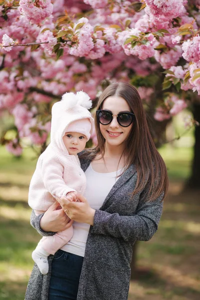 Mama cu o fetiță în parc se plimbă lângă copacul sakura — Fotografie, imagine de stoc