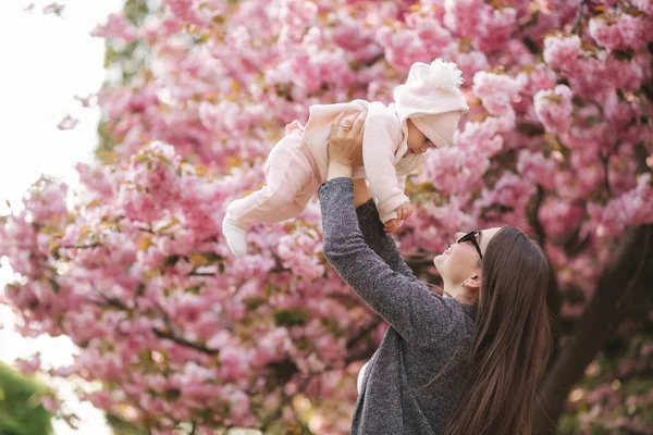 Pohled na tu šťastnou mladou matku, jak drží holčičku v dlaních a dívá se na ni s láskou — Stock fotografie