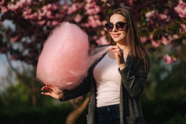 Pembe sakura ağacının önünde pamuk şeker yiyen çekici genç kızın yakın portresi