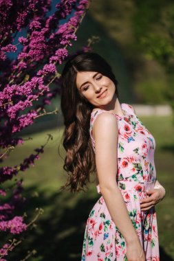 Güzel kadın mor çiçek açan ağacın yanında duruyor. Mavi arka plan. Model