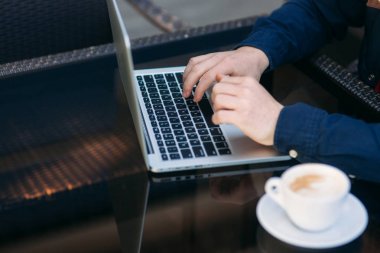 Masada dizüstü bilgisayar kullanan adamın yakın. Cam masa üzerinde Cappuchino