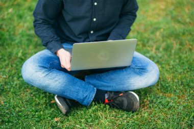 Parkta çimüzerinde oturan ve dizüstü bilgisayar üzerinde çalışmak Genç adam Orta seçim