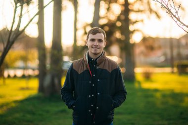 Koyu mavi gömlekli genç adam parkta fotoğrafçıya poz veriyor.