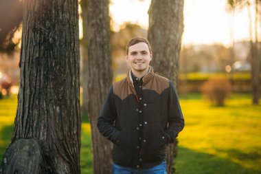 Koyu mavi gömlekli genç adam parkta fotoğrafçıya poz veriyor.