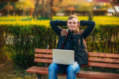 Genç iş adamı parktaki dizüstü bilgisayarını bitiriyor. İnternette çalışıyorum. Çevrim içi iş