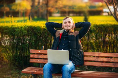 Genç iş adamı parktaki dizüstü bilgisayarını bitiriyor. İnternette çalışıyorum. Çevrim içi iş