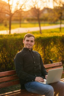 Genç işadamı parkta dizüstü bilgisayarla çalışıyor.