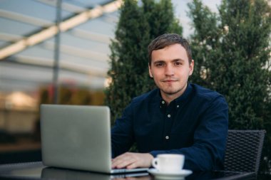 Genç adam laptopuyla ve işiyle kafede oturuyor. Fedai haberleri var. Cappuchino masada.