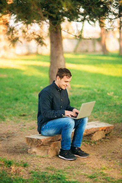 Programmer working in the park on laptop. Man sitting on bench
