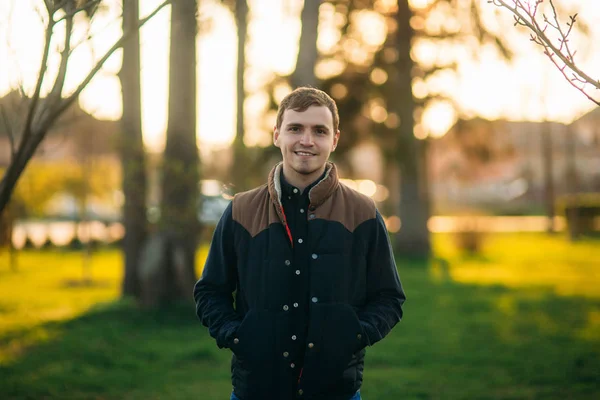 Koyu mavi gömlekli genç adam parkta fotoğrafçıya poz veriyor.