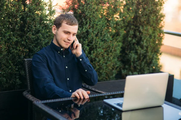 Молодий бізнесмен дзвонить комусь і використовує ноутбук у кафе. Щасливий молодий чоловік — стокове фото