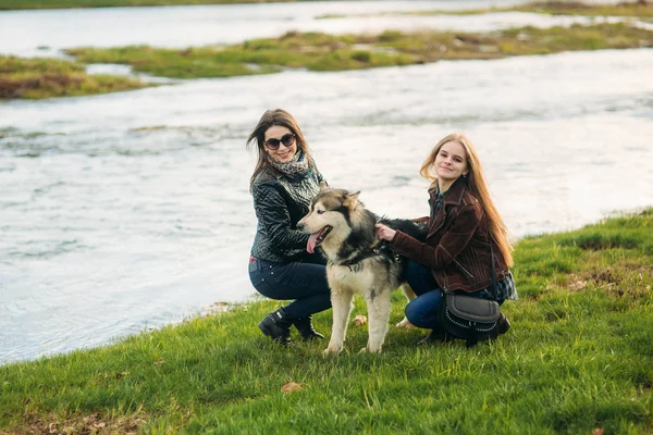 Two female walk with husky dog by the river. Friend with pets
