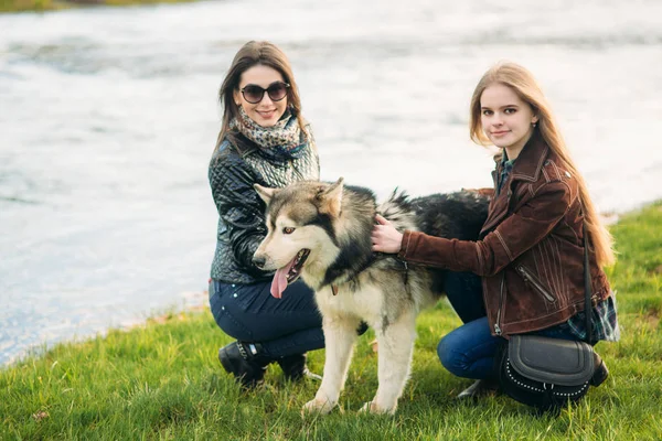 Dvě ženský procházky s huskym psem u řeky. Přítel s domácími mazlíčky — Stock fotografie