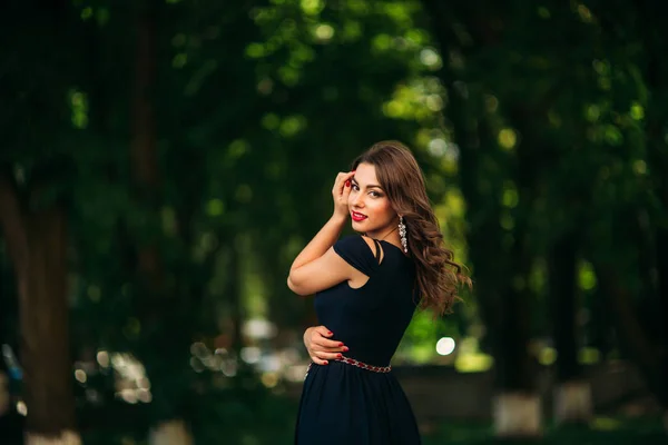 Prachtige vrouw in donker blauwe jurk staan voor groene achtergrond in het Park — Stockfoto