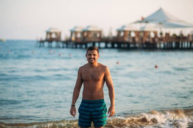 Gün batımında sahilde yürüyen yakışıklı bir adam. Güzel denizin arka planı