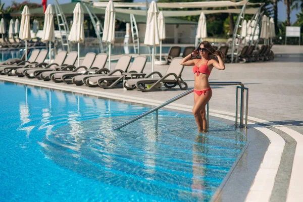 Attraktive junge Frau im rosafarbenen Bikini beim Aussteigen aus einem Schwimmbad. schöne lange Haare gebräunt weiblich — Stockfoto