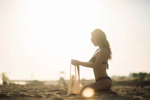 Seksi kız bir kumsalda güneşlenme ve kum ile çalış — Stok fotoğraf