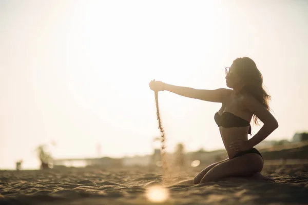 Sexy chica tomando el sol en una playa y juega con la arena —  Fotos de Stock