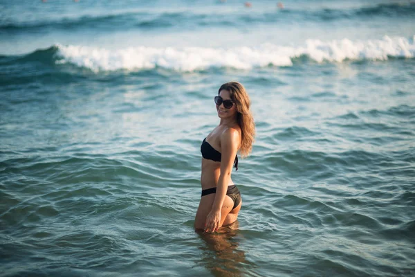 Beautiful lady is waist-deep in the sea. Sexy woman in black bikini wait for waves in the sea — Stock Photo, Image