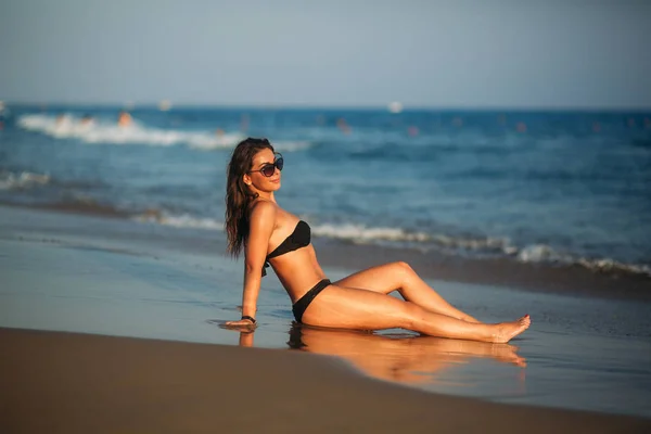 Sexy Mädchen sonnt sich an einem Sandstrand und sitzt am Meeresufer. schöne Frau an der Küste bei Sonnenuntergang — Stockfoto