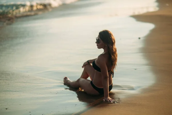 Sexy Mädchen sonnt sich an einem Sandstrand und sitzt am Meeresufer. schöne Frau an der Küste bei Sonnenuntergang — Stockfoto
