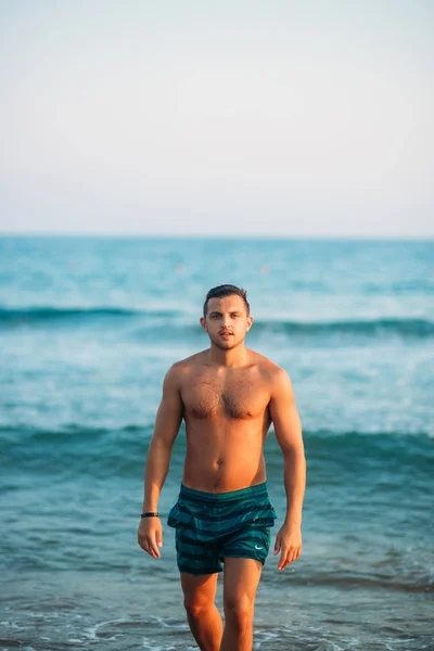 Handsome man walking on the coast in sunset. Background of beautiful sea — Stock Photo, Image