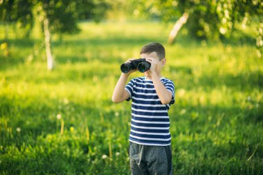 Çizgili bir gömlek küçük çocuk dürbün ile görünüyor. Bahar, güneşli havalarda