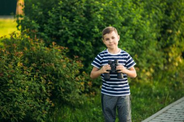 Çizgili bir gömlek küçük çocuk dürbün ile görünüyor. Bahar, güneşli havalarda