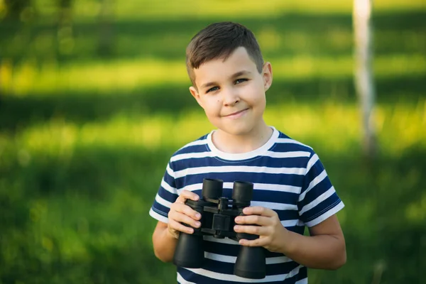 Kleiner Junge im gestreiften T-Shirt blickt durch ein Fernglas. Frühling, sonniges Wetter. — Stockfoto