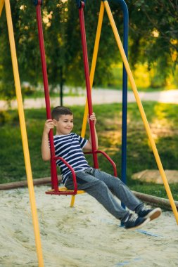 Çizgili bir gömlek içinde küçük bir çocuk oyun oynuyor, salıncakta sallanmak