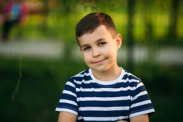 A little boy in a striped T-shirt standing in front of green background. Smiling and looking to the photographer — Stock Photo, Image