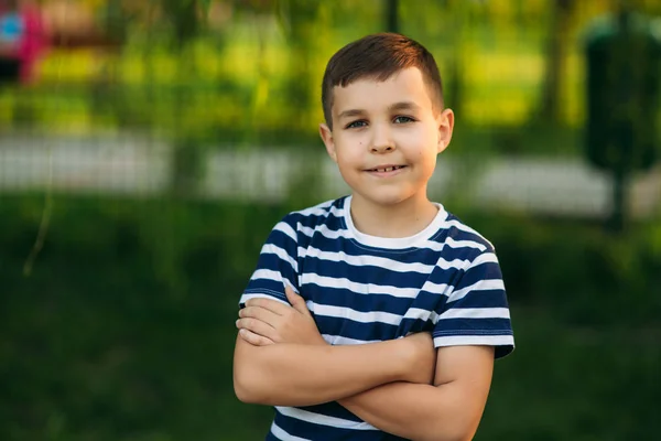 Um rapazinho com uma t-shirt listrada em frente ao fundo verde. Sorrindo e olhando para o fotógrafo — Fotografia de Stock