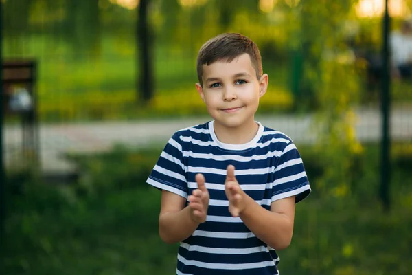 Un niño pequeño con una camiseta a rayas de pie frente al fondo verde. Sonriendo y mirando al fotógrafo. Chico golpea — Foto de Stock