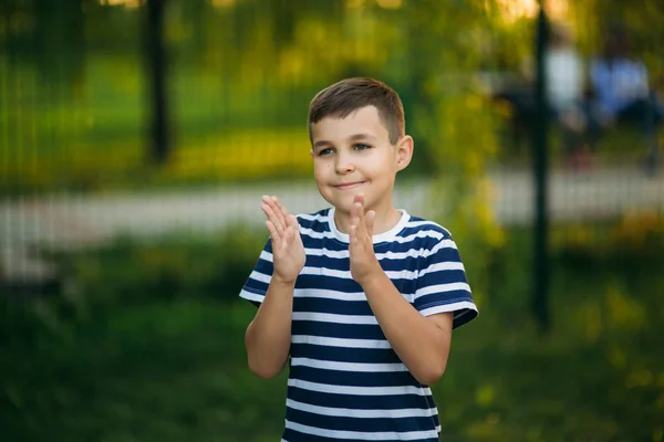 Kis fiú a csíkos póló előtt álló zöld háttér. Mosolyogva, és keres, hogy a fotós. Fiú hátrahúzódás — Stock Fotó