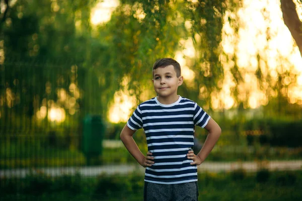 Ein kleiner Junge im gestreiften T-Shirt steht vor grünem Hintergrund. lächelnd zum Fotografen blickend — Stockfoto