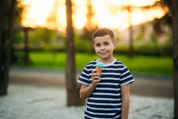 Un bambino con una maglietta a righe sta mangiando il gelato blu. Primavera, tempo soleggiato — Foto Stock