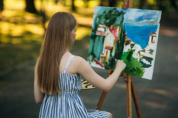Вид ззаду красива світле волосся дівчина малює картину в парку — стокове фото